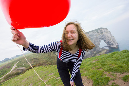 笑着的女孩带红气球以心脏的形状在风景礼仪的背图片