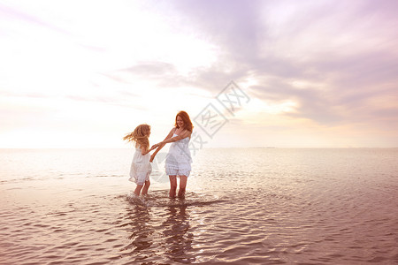 在海边快乐的周末穿着白裙子的母亲和女儿在日落时海边旋转背景图片