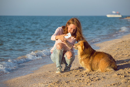 女人在海边用手机和宠物自拍图片