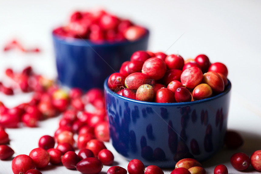 明亮的红色蔓越莓在一个漂亮的蓝色碗在一张木桌上特写图片