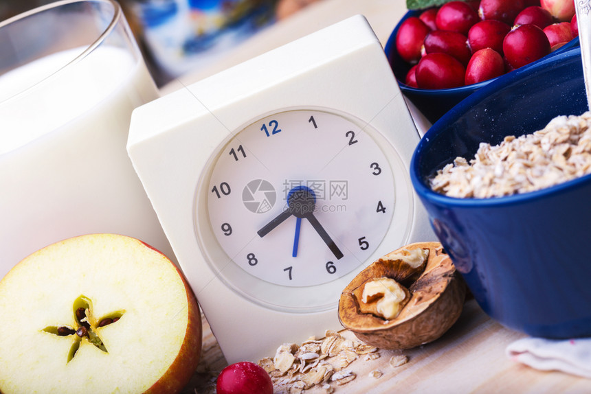 健康早餐钟表牛奶燕麦红莓坚果木桌上的苹图片