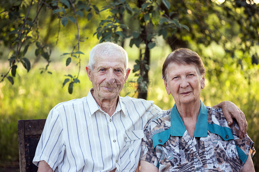 年迈老人坐在花园椅子上丈夫搂着妻子微笑的看着镜头图片