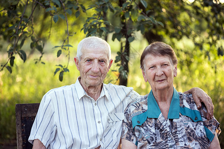 年迈老人坐在花园椅子上丈夫搂着妻子微笑的看着镜头图片