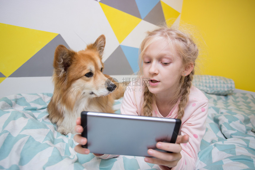 女孩和狗在床上玩平板电脑图片