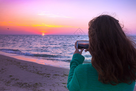 女孩在用手机拍海上日出图片