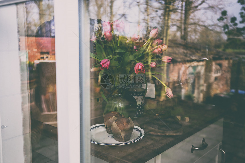 透过粉红色郁金香和纸杯蛋糕的花瓶上窗口帘视图图片