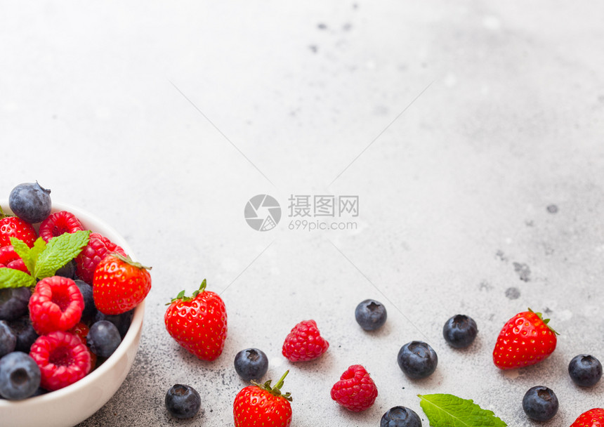 餐桌背景的白陶瓷碗中新鲜有机果子文本空间草莓蓝和薄片叶图片