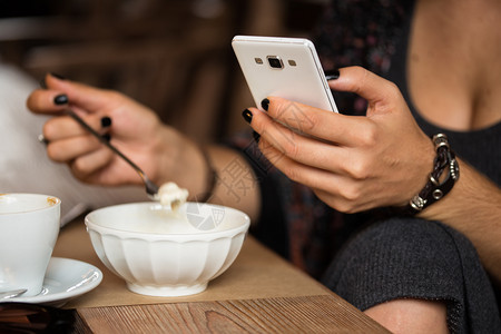 女孩用智能手机坐着喝咖啡和甜点图片