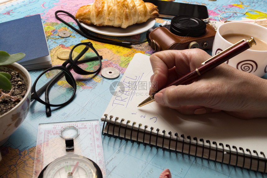 旅行计划背景旅行要带什么妇女和手和笔记本用于撰写思想复古相机钱硬币羊角面包咖啡笔指南针太阳镜智能手机图片
