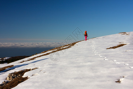 登山者在雪地和蓝天空上行走背面有云图片