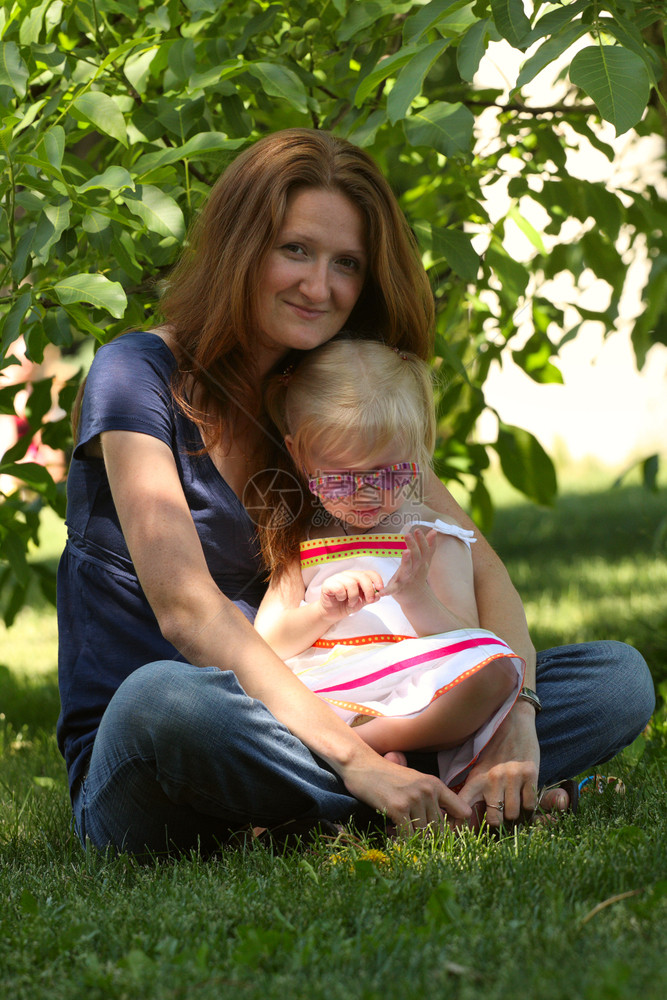 母亲和女儿坐在公园的草地上图片