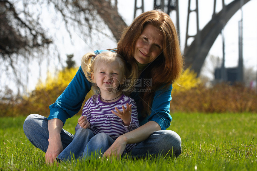 年轻母亲与女孩坐在公园的草地上图片