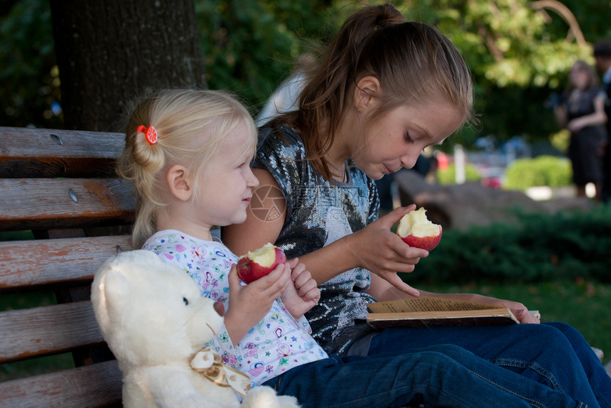 两个姐妹坐在公园的长凳上吃苹果图片