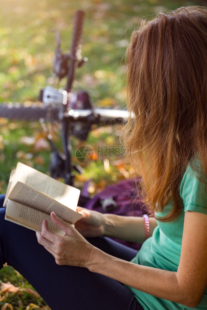 年轻女子带着自行车坐在树下看书图片