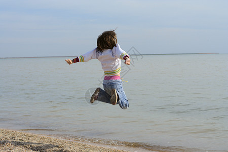 小女孩在日出时海滩上跳跃图片