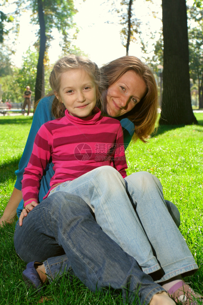 母亲笑着和她的女儿坐在公园草地上图片