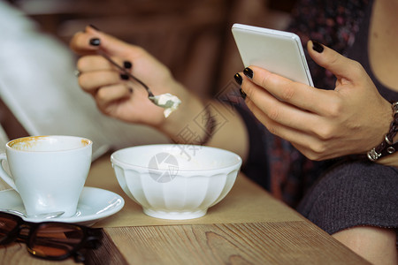 女孩用智能手机坐着喝咖啡和甜点图片