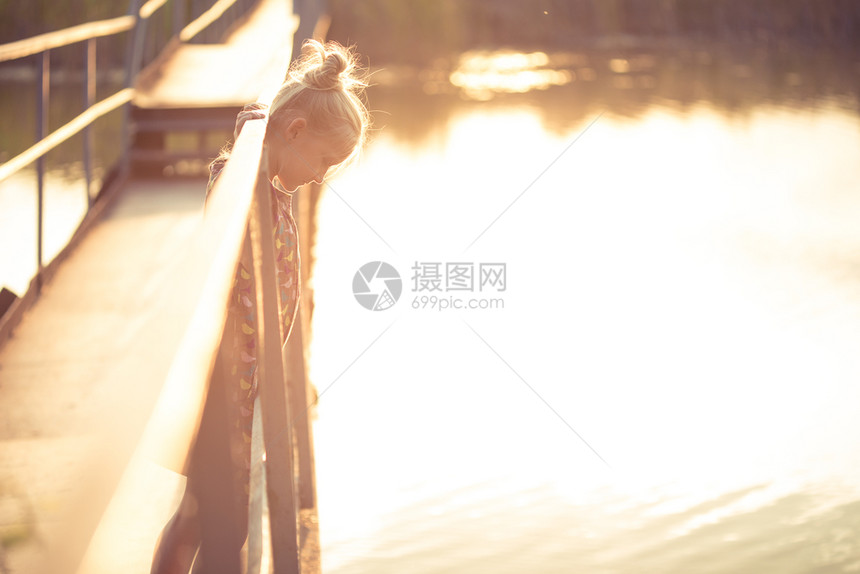 小女孩站在桥上看着日落的光束图片