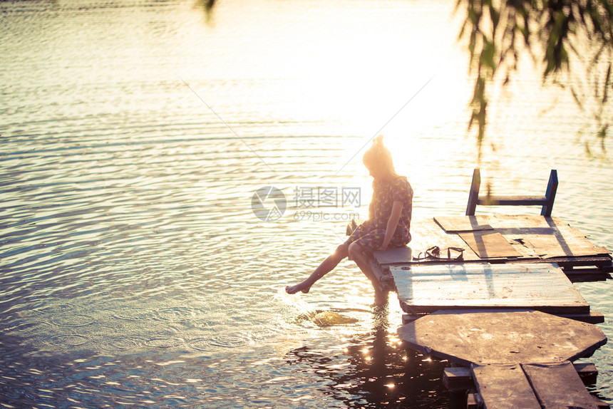 小女孩在湖边喷水日落时坐木头码上图片
