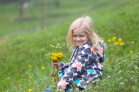 拿着花朵的金发女孩在绿草坪上图片