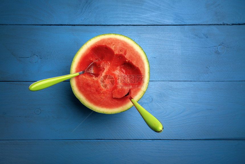 新鲜西瓜切成一半里面有两勺子蓝色背景上面有复制空间开胃的红水果美味的夏季食图片