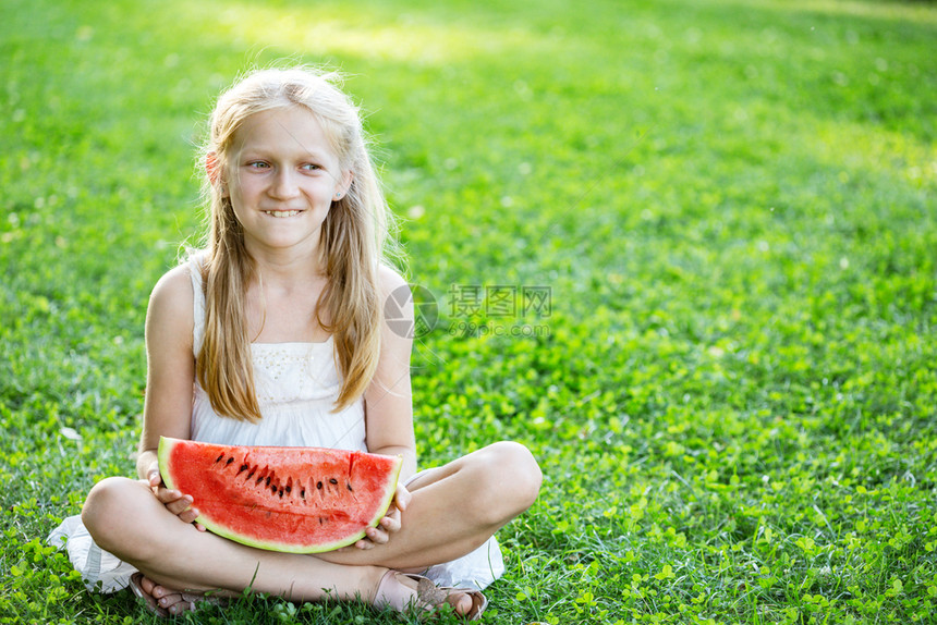 金发女孩在绿草坪上吃西瓜图片