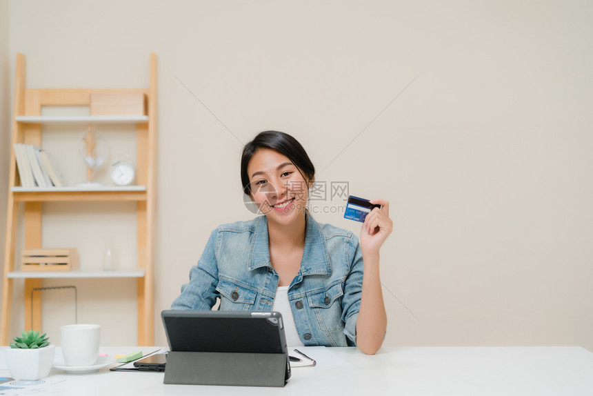 利用平板电脑信卡购买网上物身穿智能便衣坐在家中客厅的办公桌旁图片