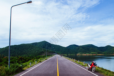 湖边街上老红色摩托车夏季天空和山丘背景高清图片