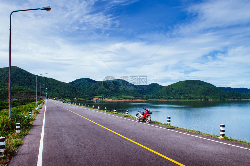 湖边街上老红色摩托车夏季天空和山丘背景图片
