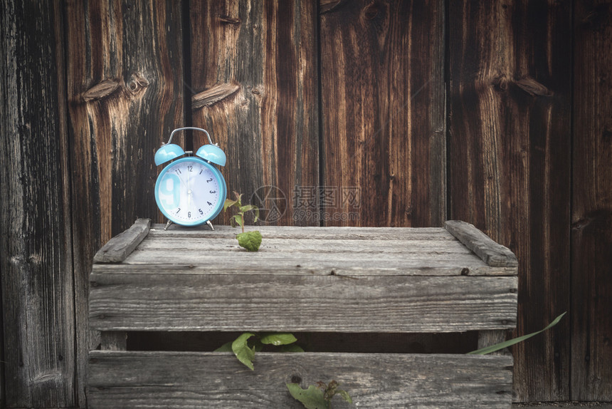 在外边一个老木箱上展示的蓝色闹钟古老图像其背景是被风吹过的木墙图片