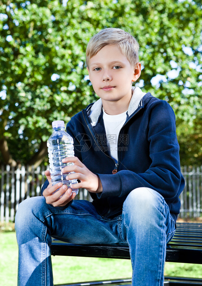坐在长椅上公园里有一瓶水的少年男孩图片