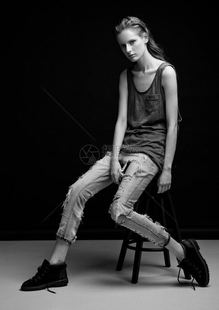 模拟测试年轻漂亮的时装模特身着牛仔裤和衬衫坐在灰色背景的椅子上图片