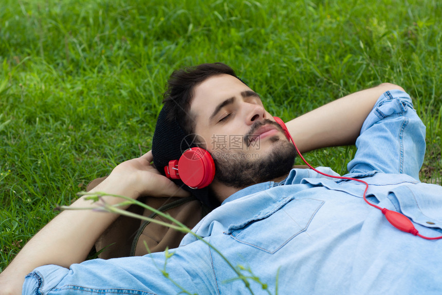年轻人用耳机在绿草上放松休闲概念图片