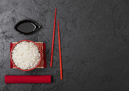 红碗加煮的有机巴斯马提茉米饭红筷子和甜豆酱加竹制地垫红皮巾加黑石本底图片