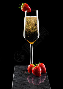 高雅的黄色香槟杯子上面有草莓黑色大理石板上有新鲜的莓子图片
