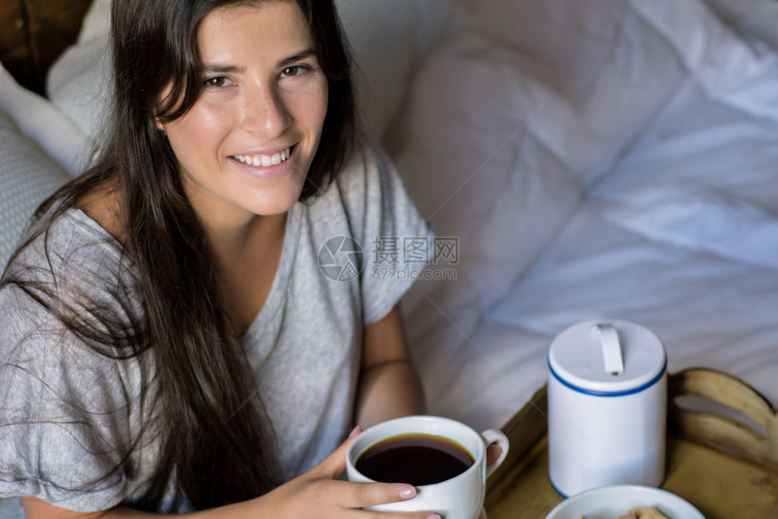 年轻女在床上吃早餐和喝咖啡图片