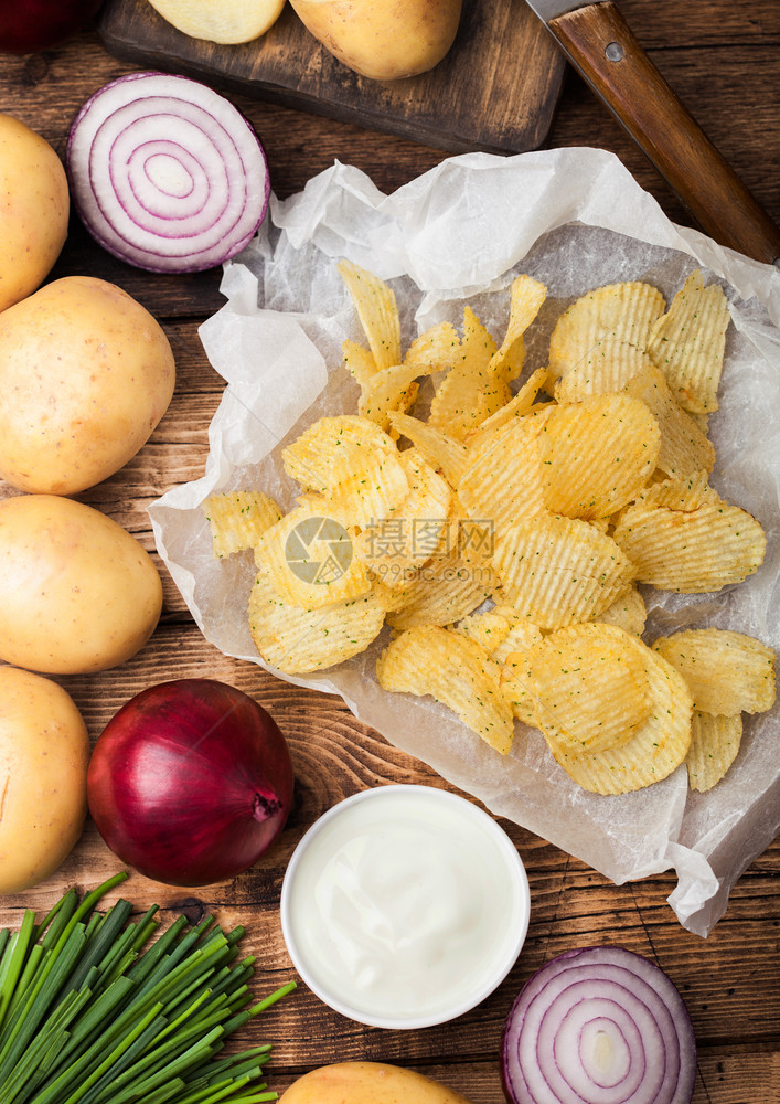 新鲜自制土豆薯片配有酸奶油红洋葱和木制桌底的香料图片