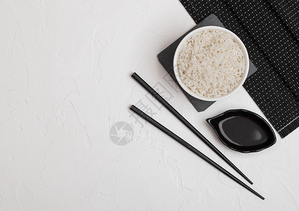白碗加煮的有机巴斯马蒂茉米饭黑筷子和甜豆酱放在竹子垫上的白底图片