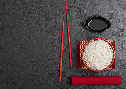 红碗加煮的有机巴斯马提茉米饭红筷子和甜豆酱加竹制地垫红皮巾加黑石本底背景图片