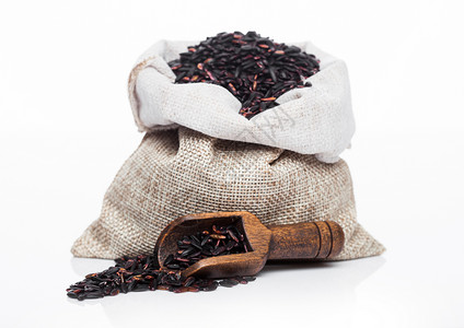 白底的原有机黑葡萄干米的木制勺子和麻布袋背景图片