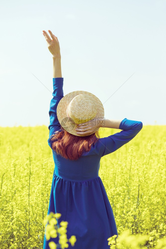 穿着帽子的快乐女孩在乡村的黄色强暴种子田野中行走图片