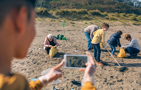 清理海滩后男孩给一群志愿者拍照背景图片