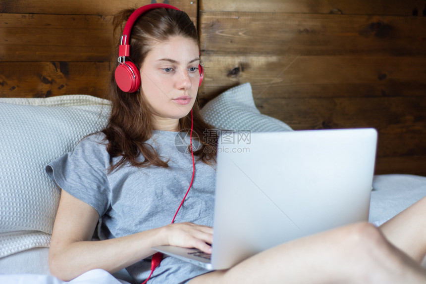 青年妇女在舒适的床上戴着耳机使用笔记本电脑图片