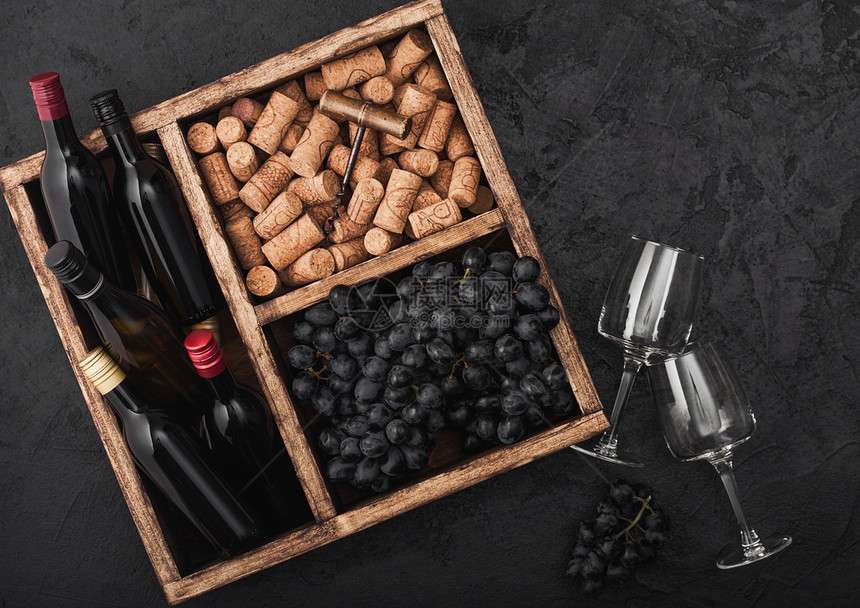 黑石背景的旧木箱内装有软和开瓶器的黑葡萄和深的空杯子图片