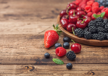 背景蓝黑素材浅木制桌底的圆质盘中新鲜的有机夏季果子混合物草莓蓝黑和樱桃背景