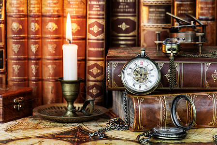 古老的口袋手表和在旧的烛台烧蜡都在古董书的背景上图片