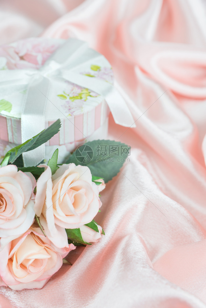 粉红玫瑰和礼物盒在丝织背景的垂直图象上放弓图片