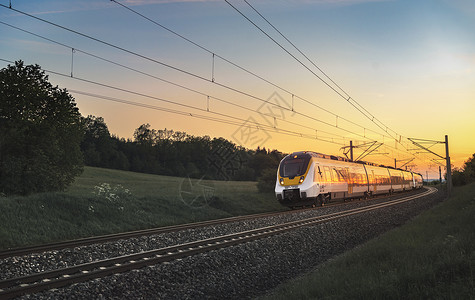现代区域列车在铁路上高速行驶穿越自然景观日落时高清图片