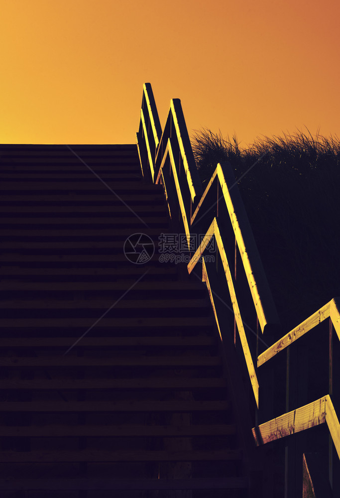 低光金色时在沙滩的木制楼梯下在高草的沙丘上爬楼梯图片