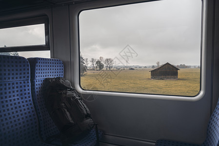 车内列蓝色椅子上有黑背包火车窗上有木屋秋季旅行概念图片